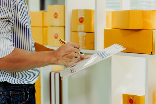 Young Asian male stock controller scanning barcode on package box to update digital store inventory system on shelves backdrop.