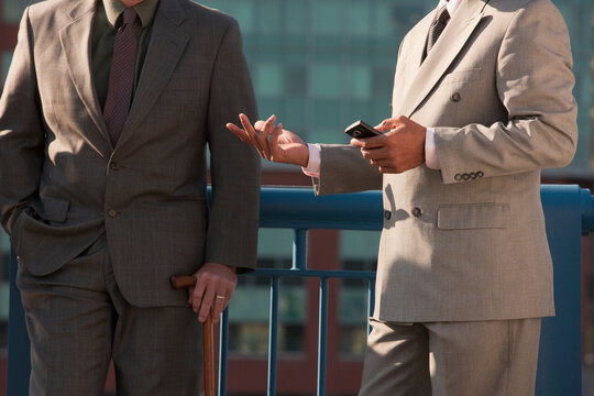 Businessmen standing together, one holding a cane and one holding a smart phone
