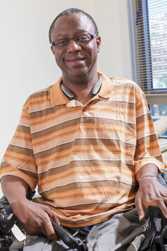 Happy man with Guillain-Barre Syndrome holding a TV remote in his power chair at home