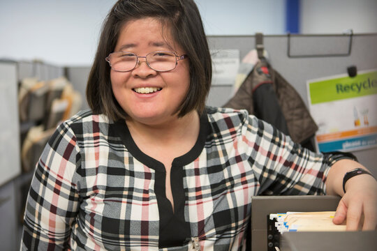 Asian woman with a Learning Disability using a file cabinet in office