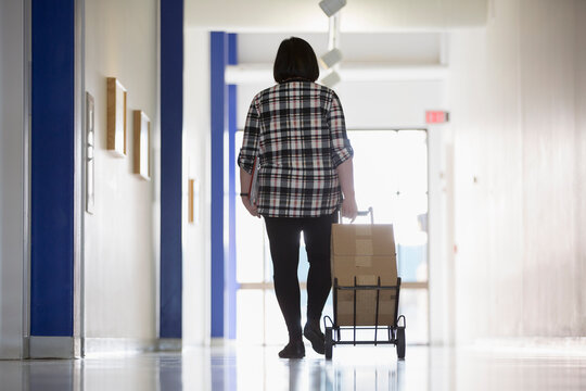 Asian woman with a Learning Disability taking boxes down an office hallway