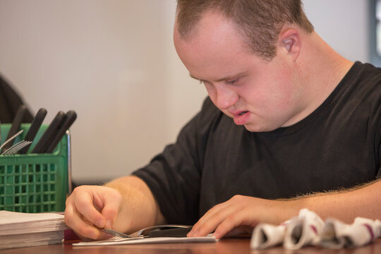 Waiter with Down Syndrome preparing napkin and silver in a restaurant