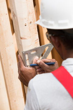 Hispanic carpenter measuring house frame with a rafter square