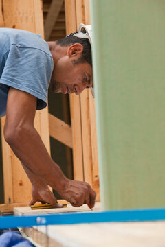 Hispanic carpenter marking a measurement on a board at a house under construction