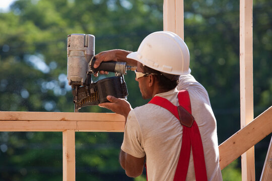 Hispanic carpenter using a nail gun on a window frame