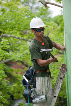 Hispanic carpenter hammering exterior sheathing on the upper floor of a house