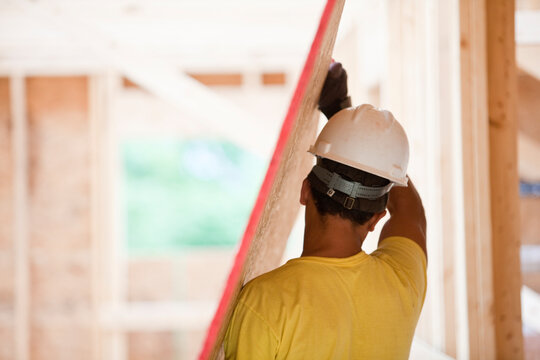 Hispanic carpenter carrying sheathing at a house under construction