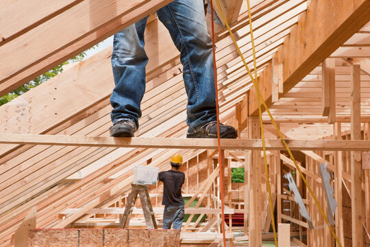 Hispanic carpenters pulling up air hose while standing on support board at a house under