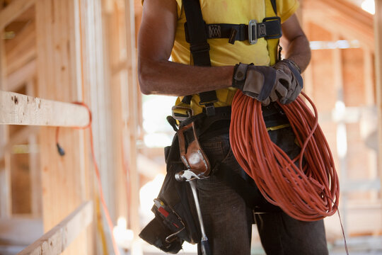 Hispanic carpenter coiling electrical power cord at a construction site