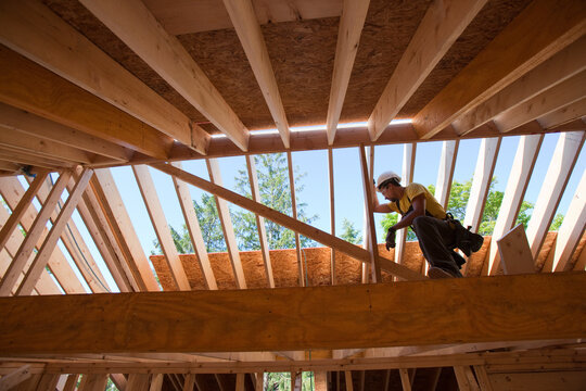 Hispanic carpenter using circular saw on rafter at a house under construction