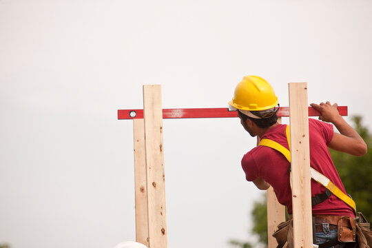 Hispanic carpenter measuring chimney posts with a level at a house under construction