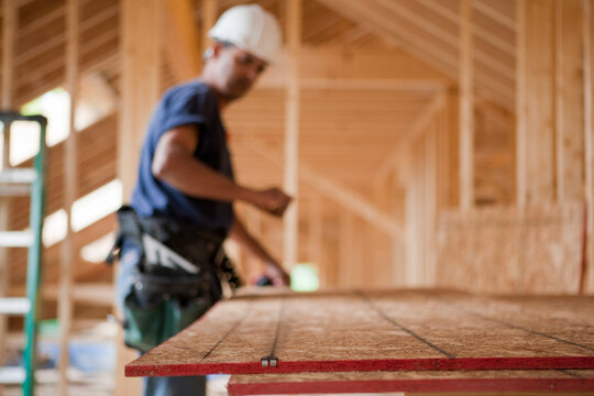Hispanic carpenter snapping a string line on a roof panel at a house under construction