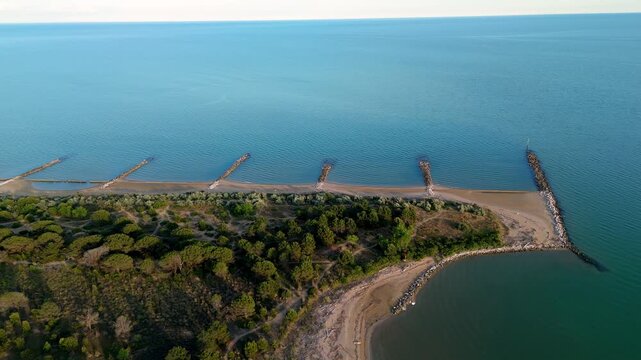High angle drone perspective of stone jetty breakwaters cutting into the calm sea along the sandy beach of Eraclea Mare at sunset, near the Piave river mouth, Veneto, Italy