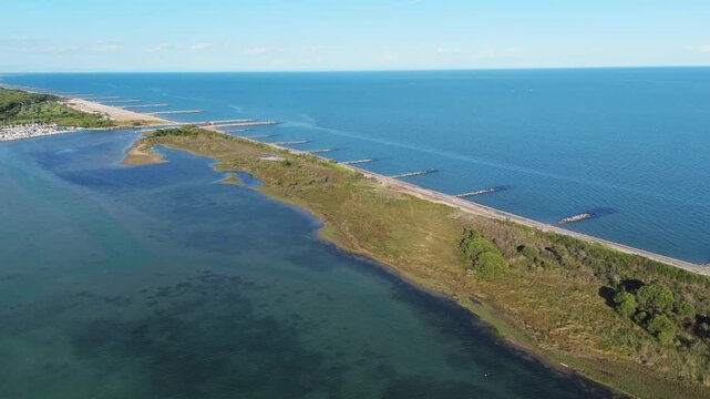 aerial drone panorama tracking the thin sandy peninsula separating green lagoon salt marshes from calm open sea waters at sunset near Eraclea and the Piave river mouth, Italy