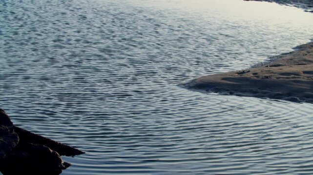 Close up established shot of the shimmering sea surface ripples reflecting a warm orange sunset glow near the Piave river estuary on the Venetian Lagoon coast, calm marine landscape, Italy.