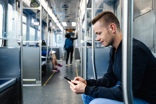 Passenger sitting in commuter train looking at mobile phone screen during daily ride. Public transport, urban lifestyle, smartphone technology and digital connectivity concept.