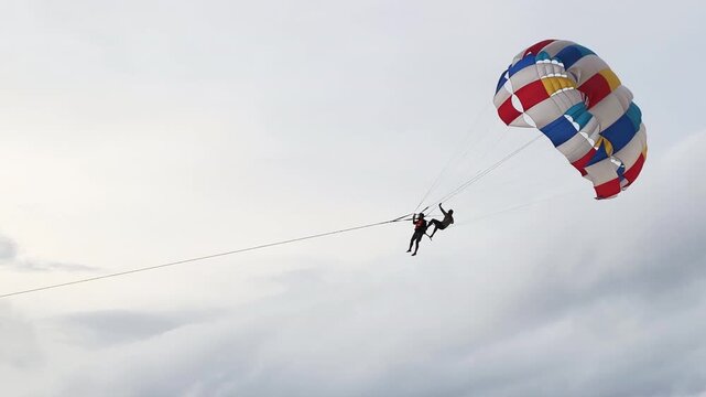 Exciting tandem parasailing flight showcases instructor and tourist high in sky. Brave duo enjoys incredible tandem parasailing flight over beautiful tropical coastline during amazing summer vacation.