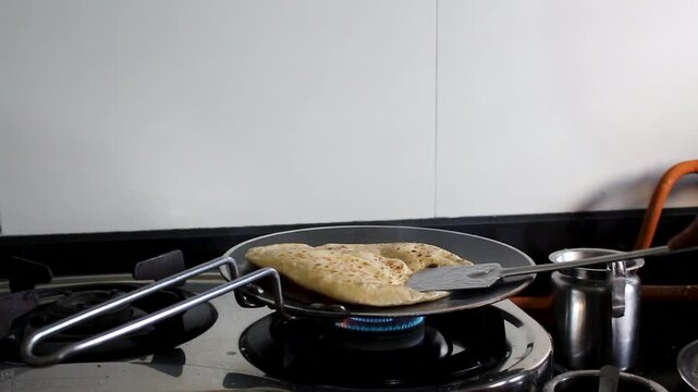 Fresh paratha roasting directly over a gas flame in an Indian kitchen. Ideal for home cooking, breakfast preparation, traditional food, culinary culture, and meal preparation content.