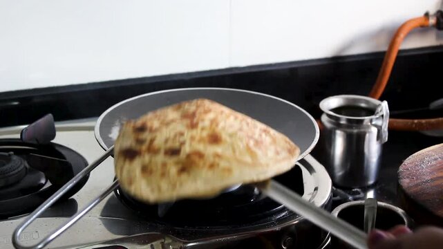 Close-up of fresh paratha being cooked and flipped on a gas stove. Ideal for Indian cuisine, home cooking, food preparation, traditional meals, and kitchen lifestyle projects.
