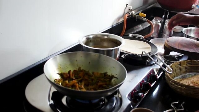 Cook prepares fresh chapati and vegetable curry on a gas stove in an Indian kitchen. Ideal for food service, restaurant, catering, cooking process, and hospitality concepts.