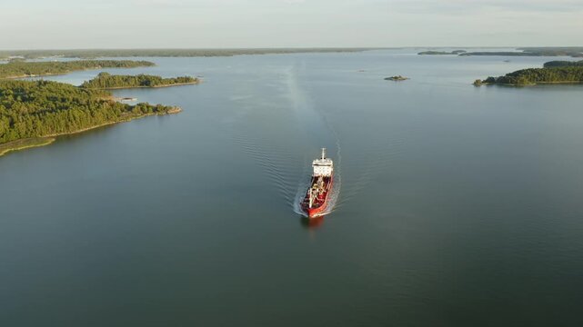 Oil and chemical tanker navigating Finnish archipelago in soft evening sunlight. Descending aerial front view.