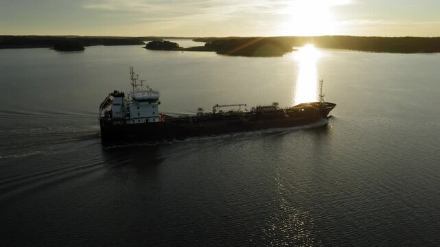 Oil and chemical tanker navigating Finnish archipelago in soft evening sunlight. Aerial side view.