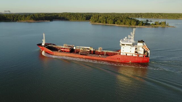 Oil and chemical tanker navigating Finnish archipelago in soft evening sunlight. Low altitude aerial side view.