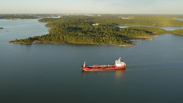 Oil and chemical tanker navigating Finnish archipelago in soft evening sunlight. High altitude aerial side view moving to front.