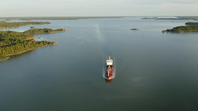Oil and chemical tanker navigating Finnish archipelago in soft evening sunlight. High altitude aerial front view.