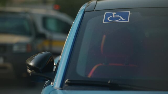 Handicap parking permit displayed on a blue parked car windshield in city street