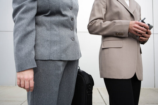 Midsection of two women holding mobile phones and suitcase