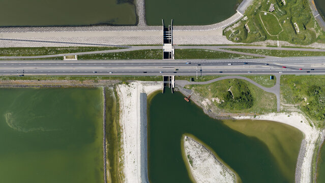 Aerial view of the Vismigratierivier fish migration river crossing the Afsluitdijk highway with green embankments and sandy shores in Kornwerderzand, Friesland, Netherlands.