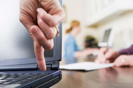 A woman's finger pointing downwards towards a key on a laptop keyboard