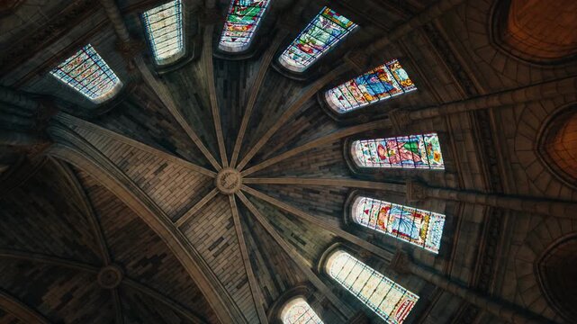 Architectural view of the ornate ceiling and stained glass windows inside a church in Bergerac, Dordogne. Low-angle perspective showcasing religious art and symmetry.