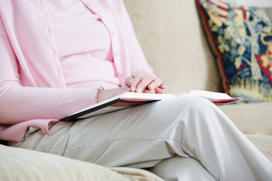 Midsection of a woman sitting on the couch with a book on her lap