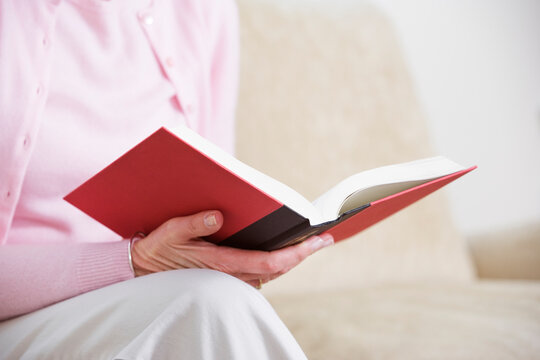 Midsection of a woman sitting on a couch and holding a book