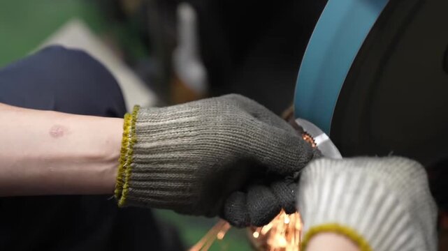 Close-up of worker hands grinding pliers on belt sander with sparks flying in factory
