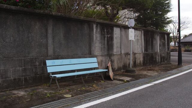 Static view of a weathered rural bus stop in Japan with a blue bench.