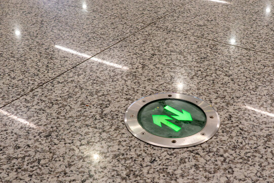 Illuminated green directional arrow floor indicator embedded in polished granite tile at modern transit station