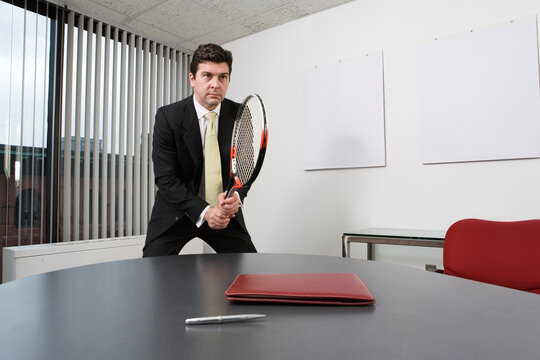 View of a business man holding a tennis racquet in an office