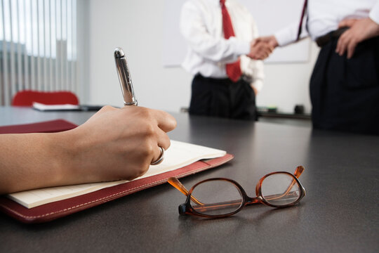 Person writing with business men shaking hands in the background