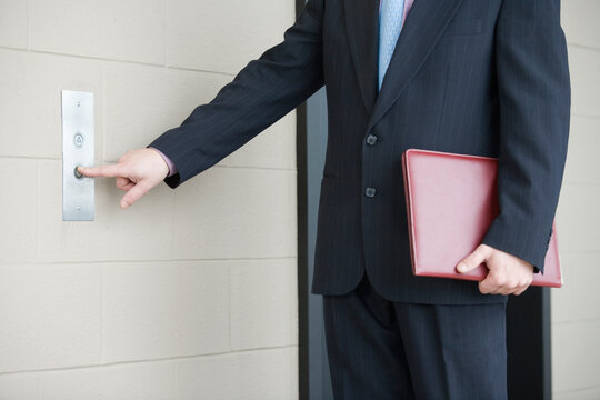 Mid section view of a businessman pressing button for elevator in an office building