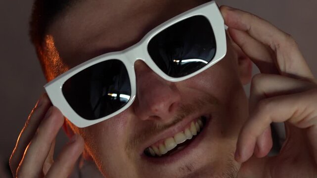 A guy wearing stylish white-framed glasses dances and rejoices in a dark room.
Good mood and dancing