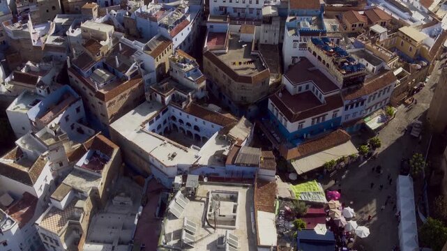 Overhead drone over Chefchaouen medina square, market stalls and kasbah tower below.