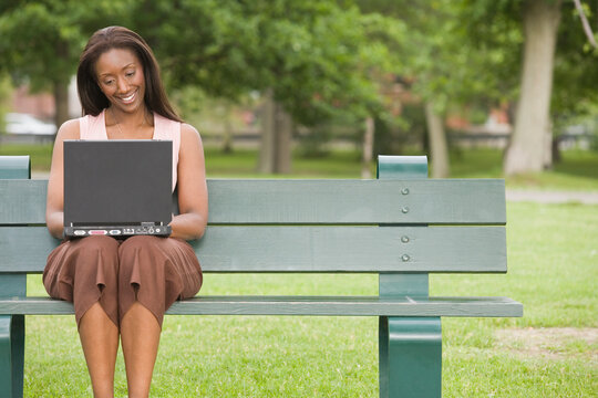 Mid adult woman sitting on a park bench and using a laptop
