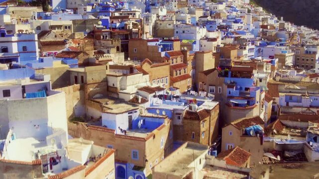 Drone pulls back low over Chefchaouen's mixed blue and ochre rooftops.