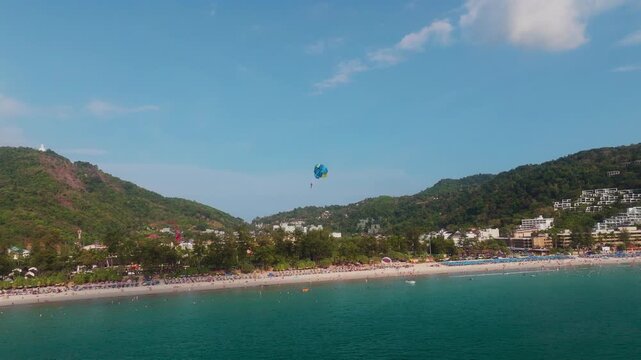 Drone pans Patong Bay as a parasail climbs between iconic twin hills, Phuket