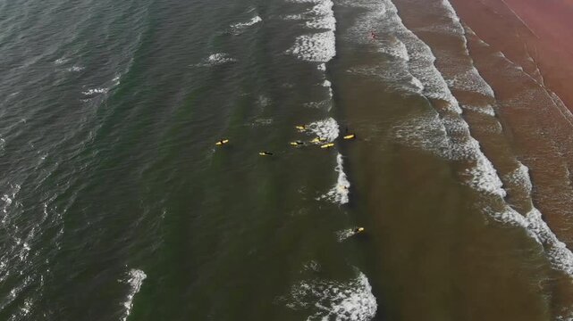 Drone spins and pulls back revealing surfers and Moroccan red sand beach