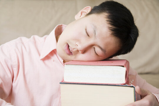 Close-up of a teenage boy sleeping on a stack of books