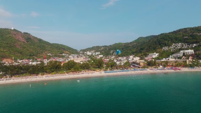 Drone hovers over turquoise sea as a parasail rises above iconic Patong Beach